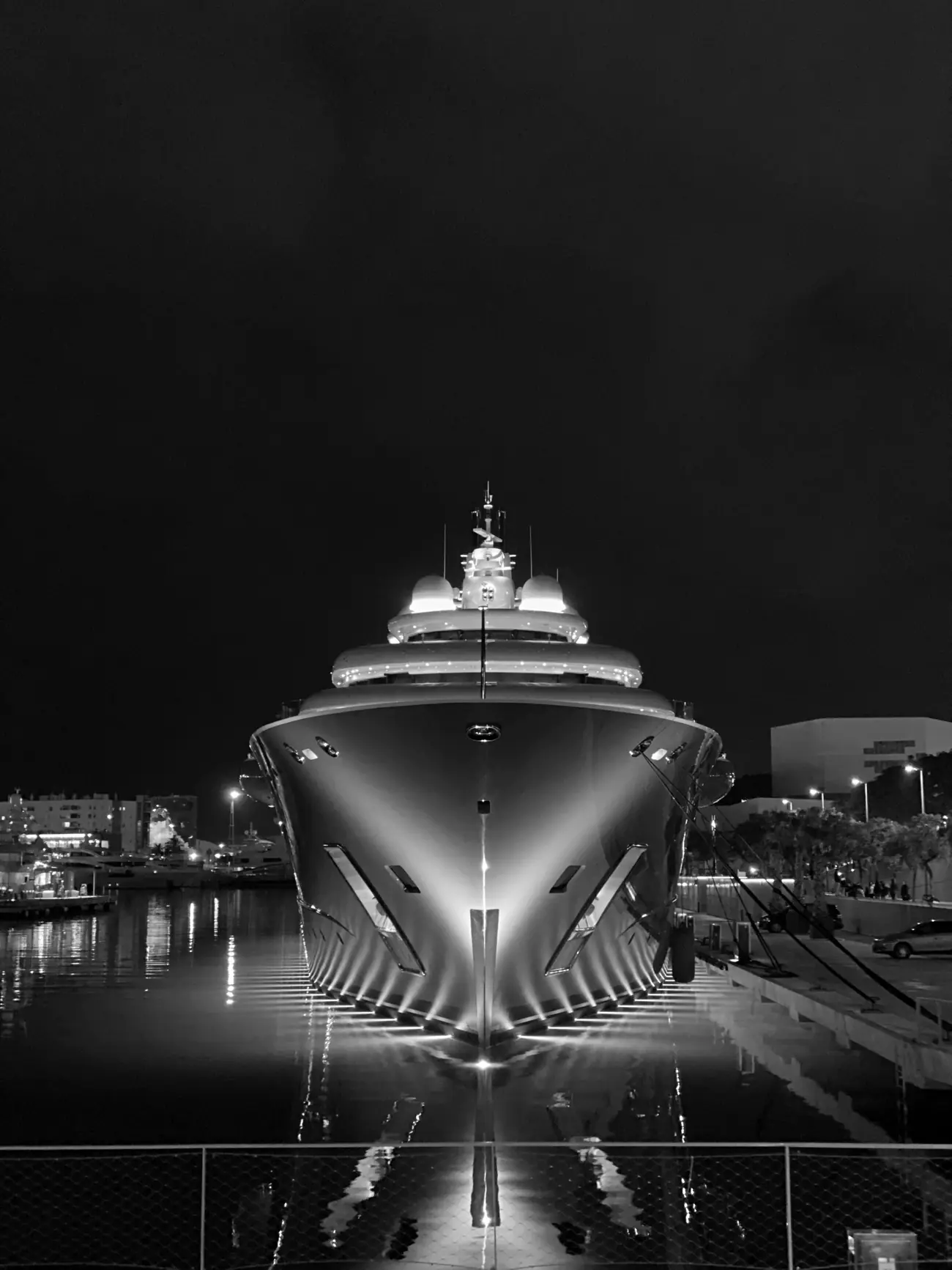 A megayacht’s bow at night, lit and reflected on the quay