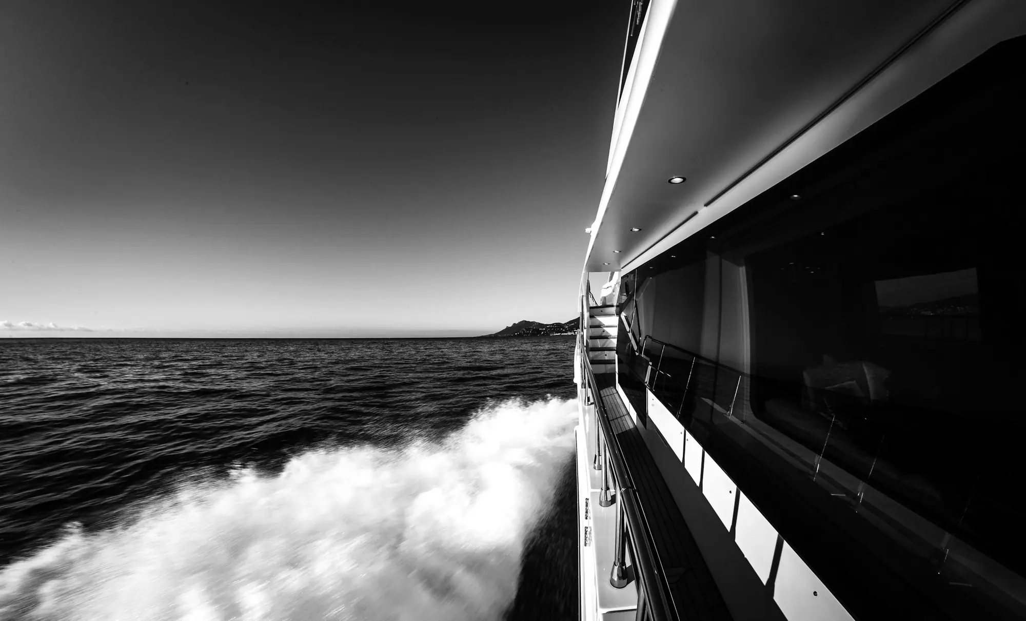 The side of a superyacht at speed, its wake behind it